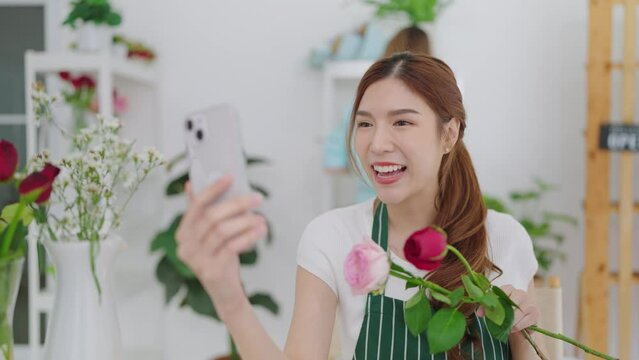 Young asian women owner floral store holding rose flowers on hands showing to client choosing through video call on smartphone for taking order. Small business concept
