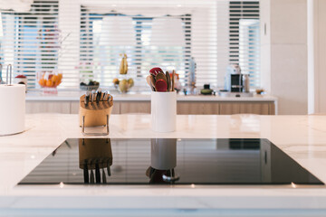 Detail of marble worktop with ceramic hob and colorful wooden kitchen utensils and knife set in a...