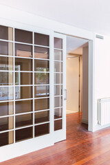 Wooden sliding door and glass in a bright living room with dirty parquet floor with construction dust