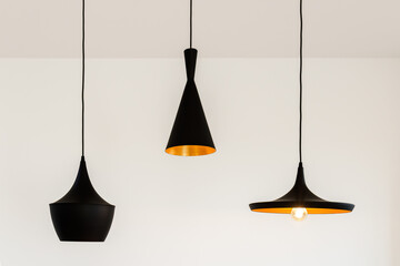 Three lighted black metal lamps hanging from the ceiling on a plain wall