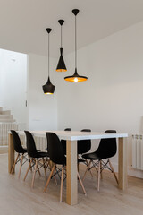 Dining room with white and wood table and six black chairs with three black metal lamps hanging from the ceiling and wooden floor - obrazy, fototapety, plakaty
