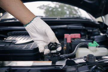 Close-up of hand of a gloved mechanic opening the radiator cap to check the coolant level. A man's...