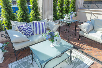 a chic terrace of a country house with wrought iron furniture, vases with flowers and columns on a bright summer sunny day
