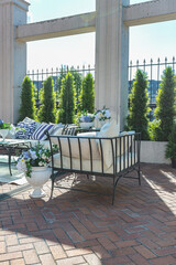 a chic terrace of a country house with wrought iron furniture, vases with flowers and columns on a bright summer sunny day