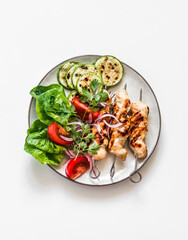 Chicken skewers, grilled zucchini, tomatoes, lettuce, red onion salad on a light background, top view
