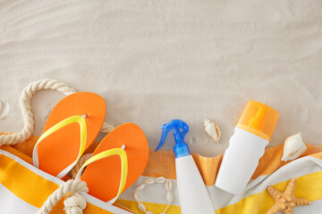 Sunblock cream concept for summer holidays. Top view shot of sunblock cream bottles, bag, beach towel, flip-flops, shell bracelet, seashells, starfish on sand background with space for ads or text