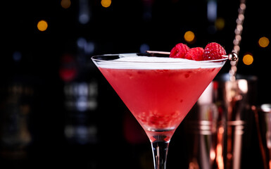 Clover club alcoholic cocktail drink with dry gin, raspberry syrup, lime juice, quail egg white and ice in glass. Black bar counter background, bar tools and bottles