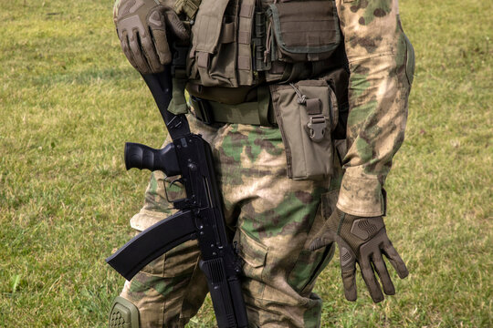 A soldier in uniform and with a weapon stands against a background of green grass