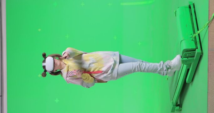Vertical shot on green screen background. VR or AR online walk. Girl walk in augmented reality googles and conducts a virtual broadcast to her audience. Walking on a treadmill at 45 degrees to camera.
