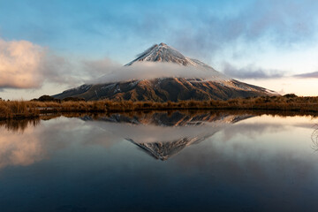 Mount Egmont, also called Mt Taranaki on the north Island of New Zealand during sunset with a beautiful reflection in the water of a little lake