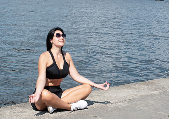 Yoga concept. A beautiful girl in a lotus position sits on the embankment by the river. Meditate...
