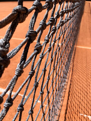 close up of a tennis net on a sunny day of a sand court, no person