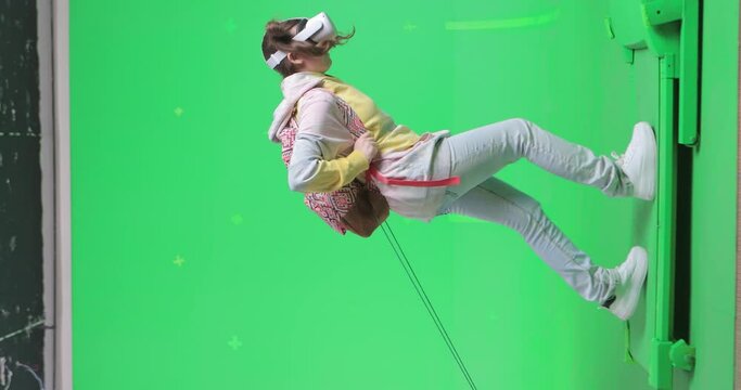 Vertical shot on green screen background. VR or AR online walk. Girl with a very heavy backpack in augmented reality headset walks through the virtual world. Walking on a treadmill side view.
