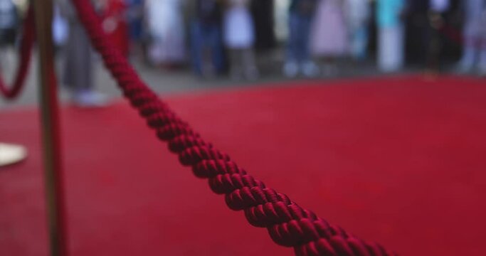 Red carpet with ropes and golden barriers on a luxury party entrance, cinema premiere film festival event award gala ceremony, wealthy rich guests arriving, outdoor decoration elements, summer day