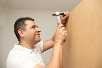 Dark-haired 40-year-old Latino repairman man works with hammer and nails on wood to fix the furniture