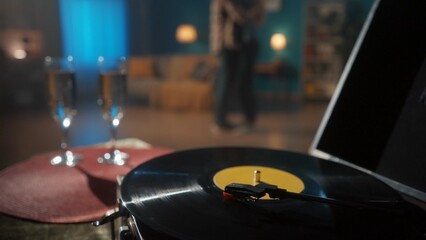 Obraz na płótnie Canvas Vintage turntable with a vinyl record close up on a blurred background of a couple dancing a slow dance. Romantic evening of a couple in love, with music and champagne, a date.