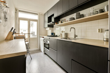 a kitchen with black cabinets and white tiles on the counter tops, along with an open window to the outside