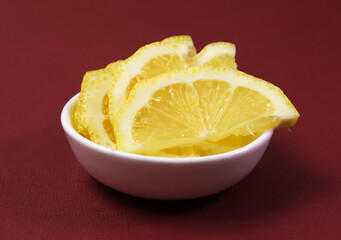 Lemon slices in a white bowl on a burgundy background. Shallow depth of field