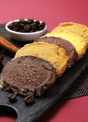 Biscuits of different flavors on a black plate with coffee beans and other ingredients on the sides. Close-up