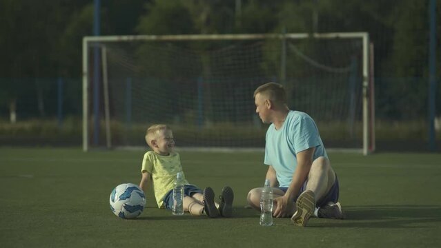 Father and his young son resting and chatting on the soccer field after practice