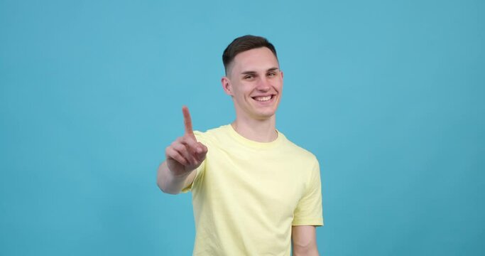 Cheerful Caucasian man is seen with a bright smile on his face. He is playfully wagging his index finger back and forth, as if gently shaking his head in a playful manner.