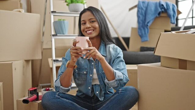 African american woman drinking coffee sitting on floor at new home
