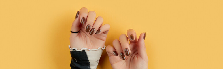 Beautiful groomed womans hands with brown nail design on yellow background