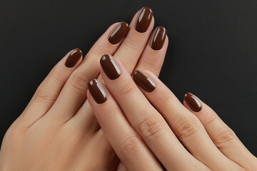 Beautiful groomed womans hands with brown nail design on black background