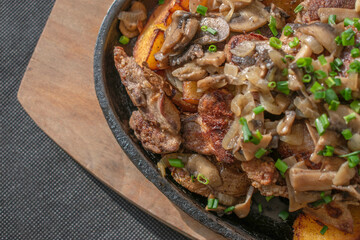 Baked chicken livers and potatoes with garlic, herbs, and fried onion in a cast iron skillet