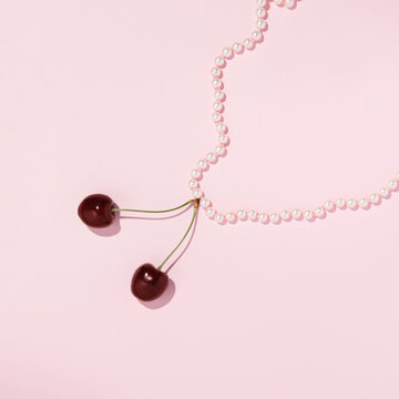 Pastel pink pearl necklace, cherry fruit pendant, creative aesthetic layout. Summer fashion trend idea. 