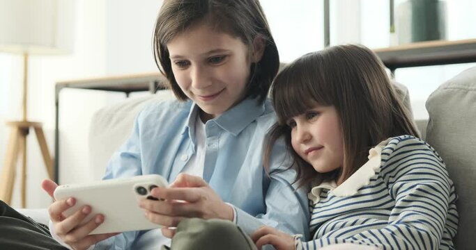 Delightful duo of brother and sister as they share laughter on the couch. With warm smiles illuminating their faces, they dive into the world of endless possibilities on their phone.