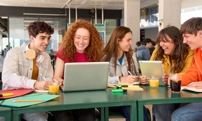 Group smiling young Caucasian college students preparing classes using laptop and tablet gathered...
