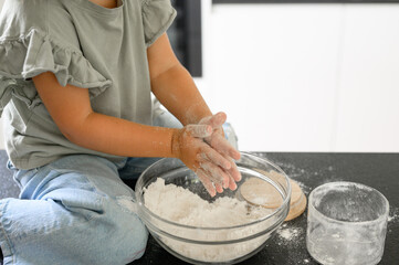 Crop child mixing dough with flour
