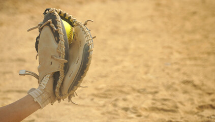 Softball being caught in a catcher's mitt with the dirt of the infield as copy space.