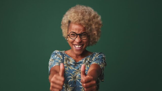 Young woman showing double thumbs up and smiles to camera isolated on blue background