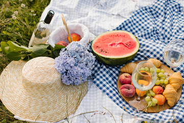 Fototapeta na wymiar Breakfast picnic with croissants, fruits and flowers on a blanket on a sunny day. Picnic, food, brunch, summer mood.