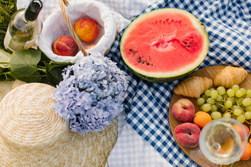 Breakfast picnic with croissants, fruits and flowers on a blanket on a sunny day. Picnic, food, brunch, summer mood.
