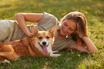 young girl hugging pembroke welsh corgi in the park in sunny weather, happy dogs concept