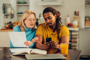 A multicultural couple is planning a budget together while holding a phone and paperwork at home. - Powered by Adobe