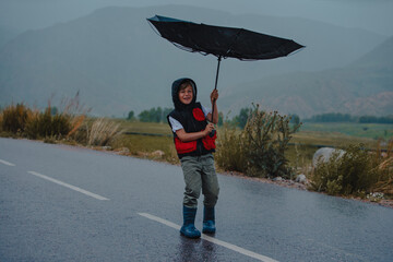 Boy standing on the road trying to hold an umbrella in rainy windy weather