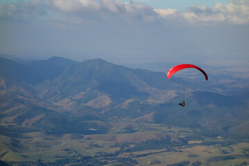 red Paraglider flying over mountain valley on a sunny clear day