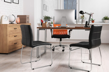 Stylish director's workplace with comfortable desk, computer and chairs for visitors in office....