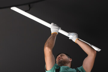 Ceiling light. Electrician installing led linear lamp indoors, low angle view