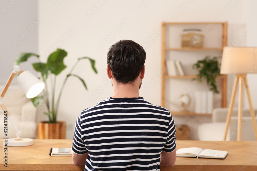 Wall mural Home workplace. Man working at wooden desk in room, back view