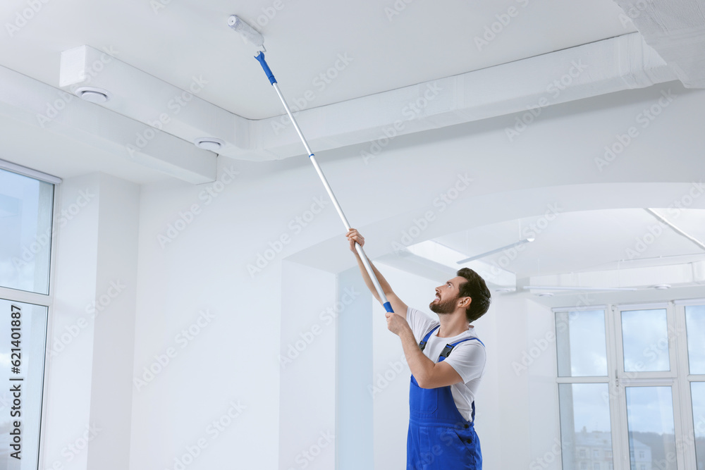 Wall mural Handyman with roller painting ceiling in room