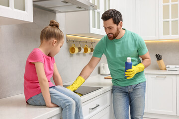 Fototapeta premium Spring cleaning. Father and daughter tidying up stove in kitchen together