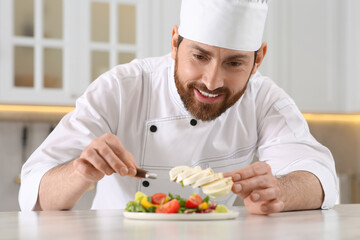 Professional chef adding mozzarella into delicious salad at marble table in kitchen