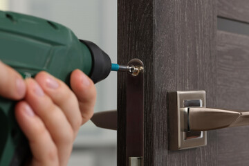 Handyman with drill repairing door lock indoors, closeup