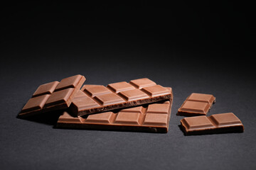 Pieces of delicious milk chocolate bars on black background