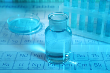 Laboratory glassware and petri dish on periodic table of elements, closeup. Color tone effect